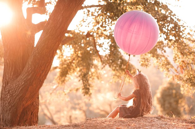 Kid girl playing with big balloon in sun light outdoors