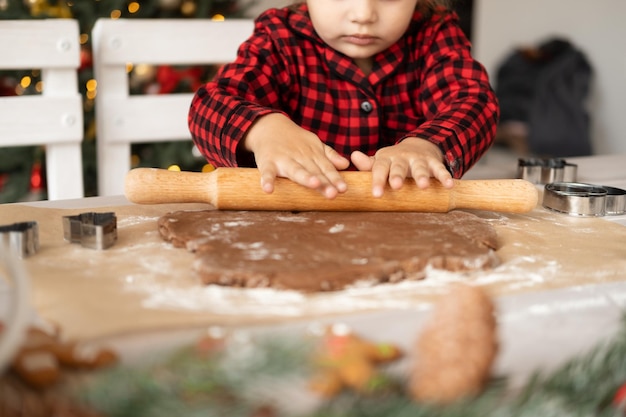 クリスマスの装飾が施されたキッチンでお祝いのジンジャーブレッドを調理する赤いパジャマの子供女の子。クリスマスクッキー