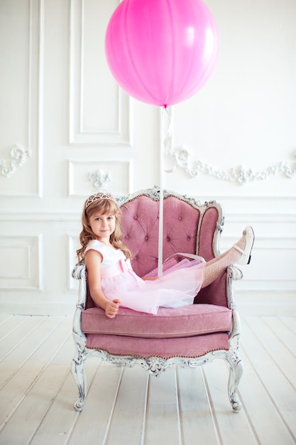 Kid girl sitting in armchair holding pink balloon