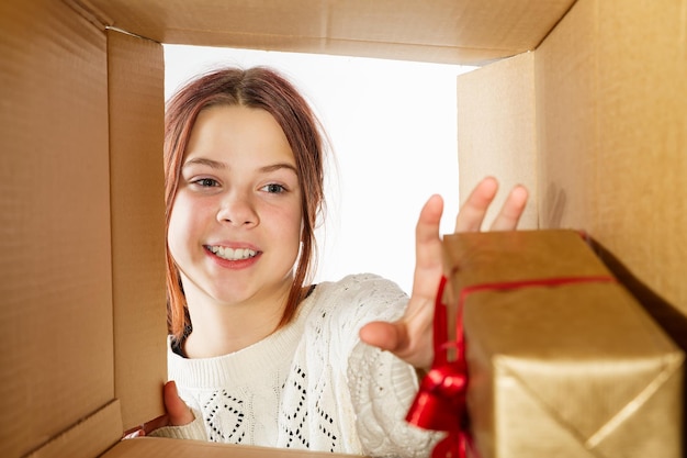 어린 소녀 십대 포장을 풀고 판지 상자를 열고 놀라움으로 안을 들여다보고 있습니다.