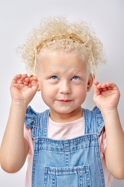 Ragazza del bambino che tocca i capelli ricci bianchi stupefacenti che sembrano pensierosi isolati su sfondo bianco ritratto ...