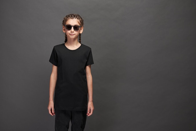 Kid girl wearing black t-shirt with space for your logo or design in studio over gray background with sunglasses