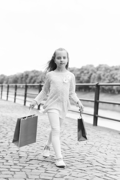 Kid girl with long hair fond of shopping fashionista girl\
shopping with pink bags girl likes to buy clothes shopping concept\
girl shopping on calm face carries shopping bags urban\
background