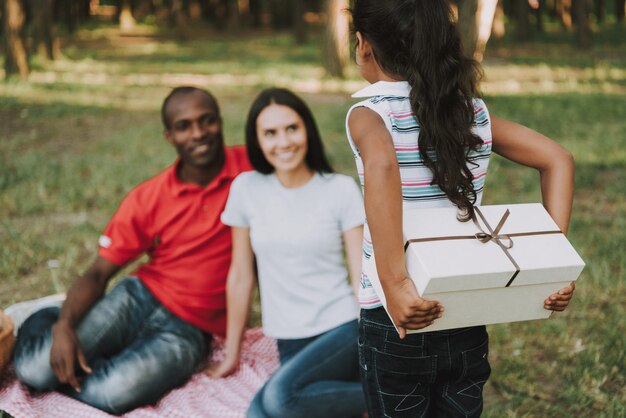 Photo kid gives present in box to parents on picnic.