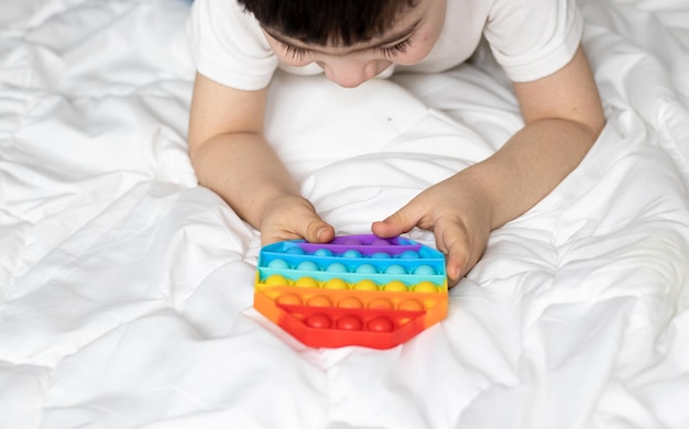 Kid hand met spelen met pop it speelgoed in regenboogkleuren blij opgewonden jongetje dat op bed ligt