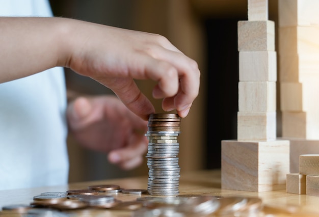 Kid hand stacking sterling pound coin and pennies nickels on wooden table with copy space