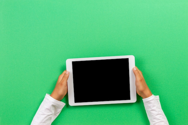 Kid handen met een witte tablet op een groene achtergrond