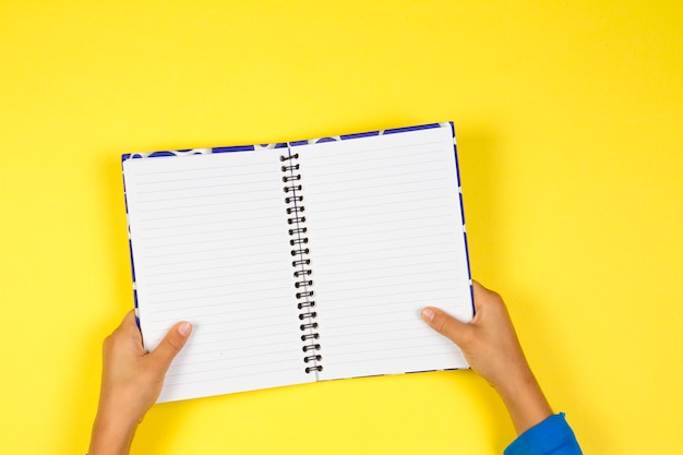 Kid hands holding open notebook on yellow background