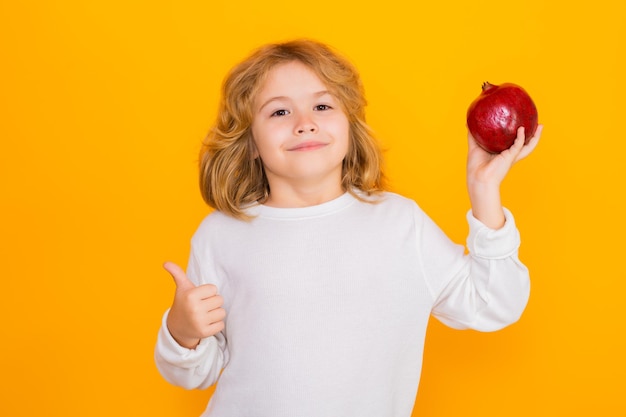 Kid hold red pomegranate in studio pomegranate fruit studio\
portrait of cute child with pomegranate isolated on yellow\
background