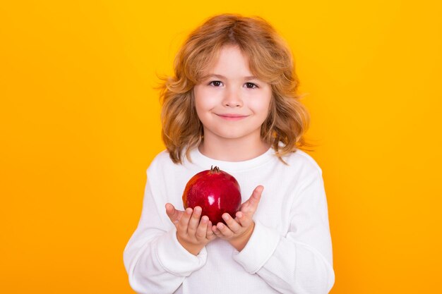 Kid hold red pomegranate in studio pomegranate fruit studio portrait of cute child with pomegranate isolated on yellow background