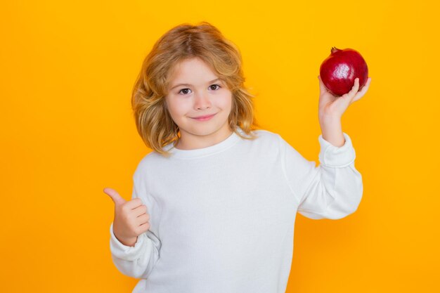 子供はスタジオで赤いザクロを保持します ザクロの果実 黄色の背景に分離されたザクロとかわいい子供のスタジオ ポートレート