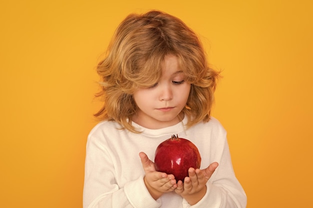 Kid hold red pomegranate in studio Pomegranate fruit Studio portrait of cute child with pomegranate isolated on yellow background