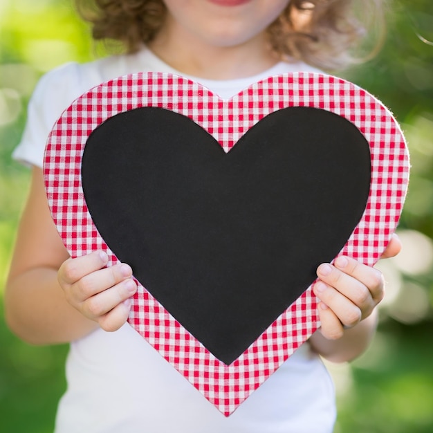 Kid holding blackboard in heart shape outdoors Spring holiday concept