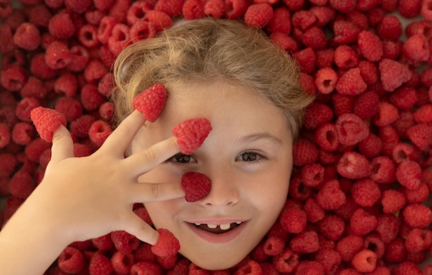 그녀의 손가락에 나무 딸기를 들고 아이 잘 익은 건강한 열매를 먹는 아이 건강한 음식과 라즈베리 공동
