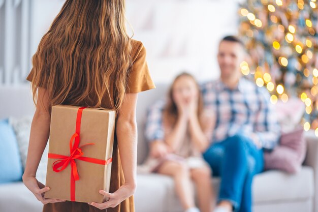한 아이가 가족의 크리스마스 트리 근처에 선물 상자를 들고 있습니다.