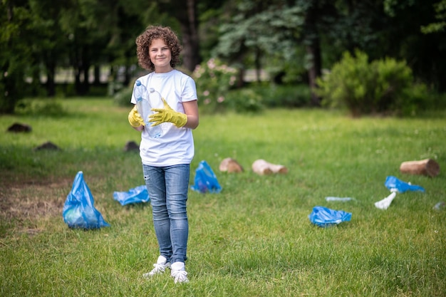 Kid in gele handschoenen in het park afval verzamelen