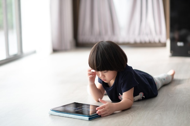 子供はタブレットに夢中ですスマートフォンを遊んでいる小さな女の子子供は電話を見て漫画を使用します