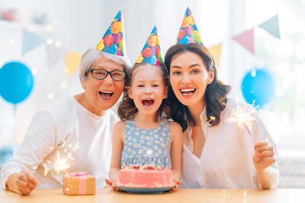 Малыш задувает свечи на торте. Бабушка, мать и дочь празднуют день рождения.