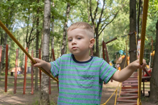 子供は遊び場でロープのつり橋に行きますかわいい男の子は登山アドベンチャーパークで活動しています