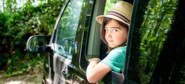 Photo a kid is sitting in a car window looking out at the trees