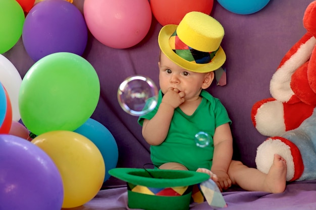 Kid is sitting in a fun festive atmosphere with balloons and watching soap bubbles.