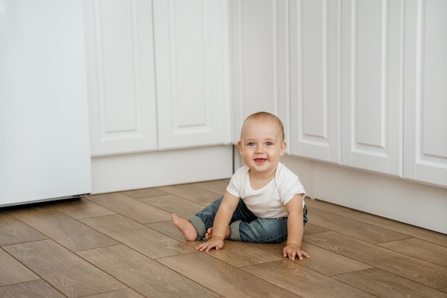 the kid is sitting on the kitchen floor and laughing