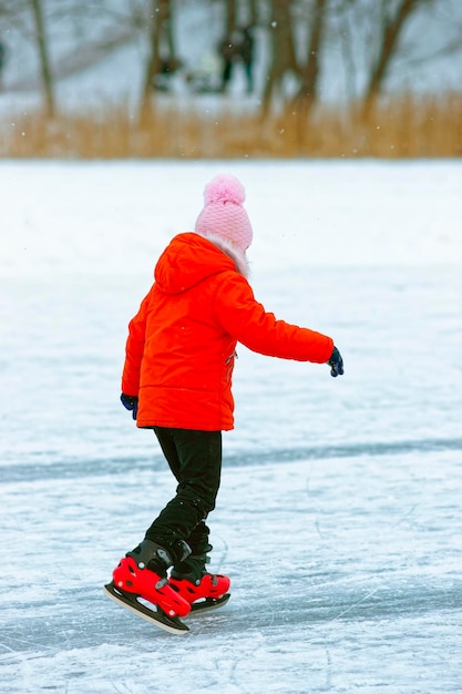 Kid is skating on the rink in winter. Skating involves any sports or recreational activity which consists of traveling on surfaces or on ice using skates.