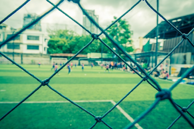 Il bambino sta allenando il calcio di calcio in sfocatura dello sfondo dietro la rete per lo sfondo e lo sfondo di allenamento sportivo di calcio e accademia di calcio