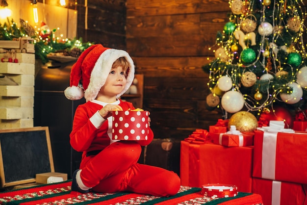 Малыш в одежде Санта-Клауса в ожидании нового года. Счастливый маленький ребенок, одетый в зимнюю одежду ...