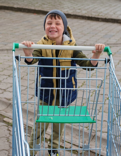 Kid jongen duwen lege winkelwagen op parkeerplaats