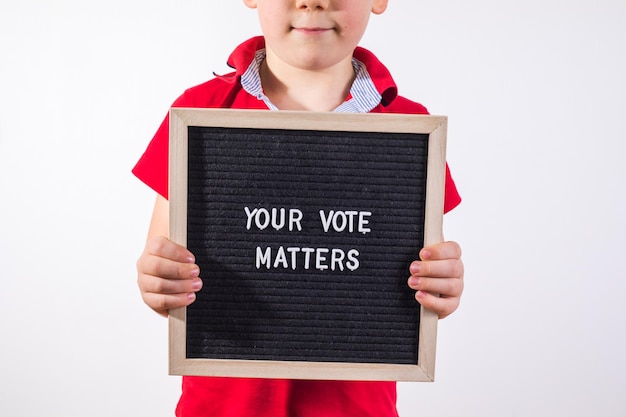 Kid jongen met brief bord met tekst Your Vote Matters op witte achtergrond