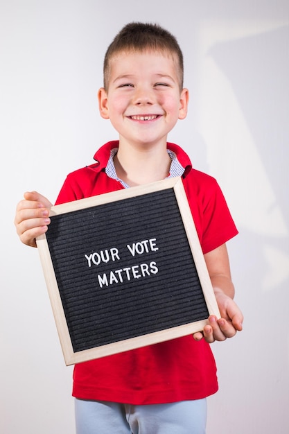 Kid jongen met brief bord met tekst Your Vote Matters op witte achtergrond