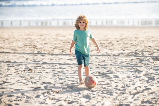 Kid jongen voetballen op zandstrand Zomervoetbal op strand voor kinderen