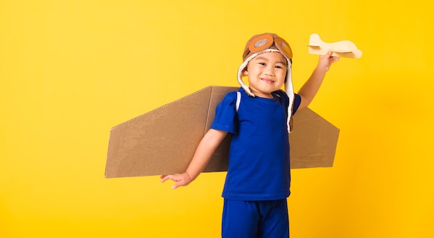 Kid jongetje glimlach dragen pilot hoed spelen en bril met speelgoed kartonnen vliegtuig vleugels