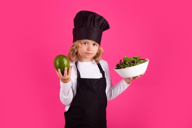 Kid kok met avocado en groente Chef jongen jongen in vorm van kok Kind jongen met schort en chef hoed een gezonde maaltijd bereiden op studio geïsoleerde achtergrond Kookproces