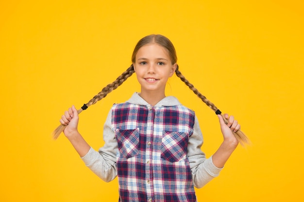 Фото Детские длинные волосы маленькая девочка в клетчатой рубашке с международным днем защиты детей маленькая девочка на желтом фоне концепция хорошего настроения положительные вибрации искренние эмоции весело милая плетеная девочка