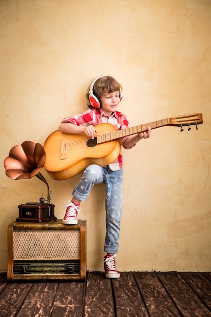 Kid luister muziek thuis. Hipster kind met retro vintage akoestische gitaar