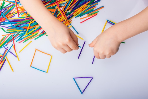 Kid making geometric shapes with colorful sticks on white background