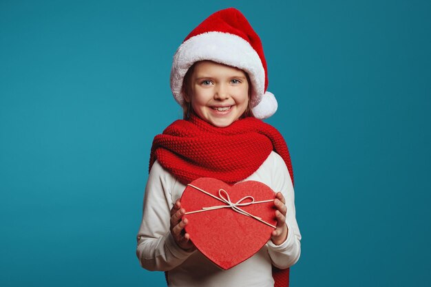 Kid meisje in kerstmuts en rode sjaal met huidige doos in de vorm van