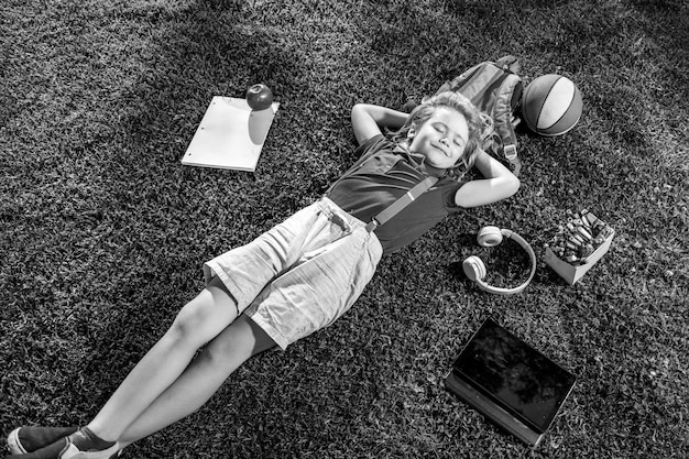 Kid met boek en taplet en rusten op het gras na school gelukkige jongen ontspannen op het gras