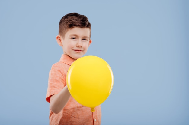 Kid met gele ballon, kijkt naar de camera, geïsoleerd op blauwe achtergrond, kopieer ruimte