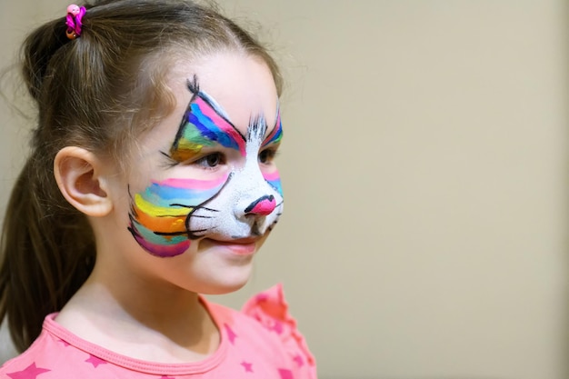 Kid met schminken van kitty schattig klein meisje met geschilderd masker op gezicht van regenboogkat