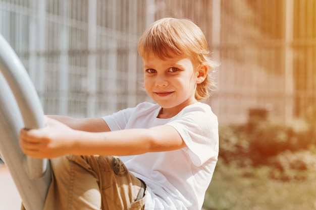 Kid op stadsspeeltuin schommels op schommel carrousel schattige kleine gelukkig lachende openhartige vijf jaar oude kind jongen met lang blond haar in een witte t-shirt generatie z kinderen geestelijke gezondheid levensstijl flare