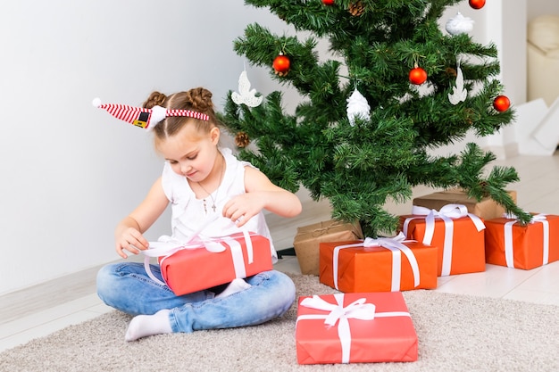 Kid opening kerstcadeautjes. Kind onder kerstboom met geschenkdozen.