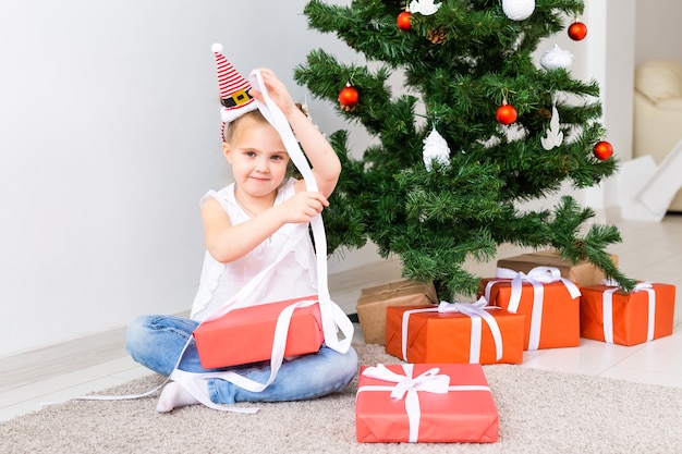 Kid opening Xmas presents. Child under Christmas tree with gift boxes.