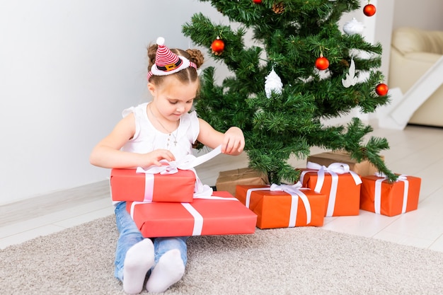 Kid opening Xmas presents. Child under Christmas tree with gift boxes.