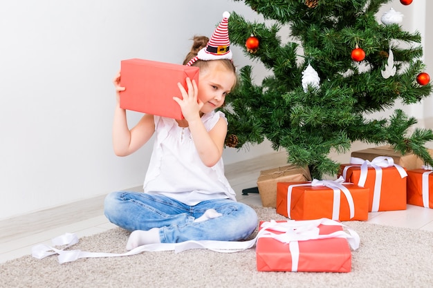 Kid opening Xmas presents. Child under Christmas tree with gift boxes.