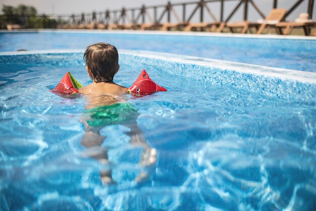 オーバースリーブの子供は夏の太陽の下で子供のためのプールで泳ぐ