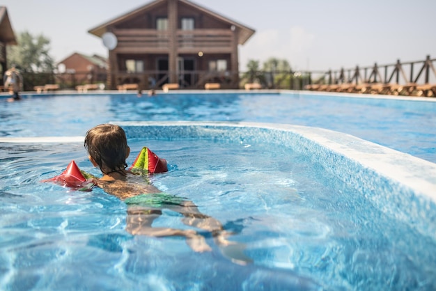 オーバースリーブの子供は夏の太陽の下で子供のためのプールで泳ぐ