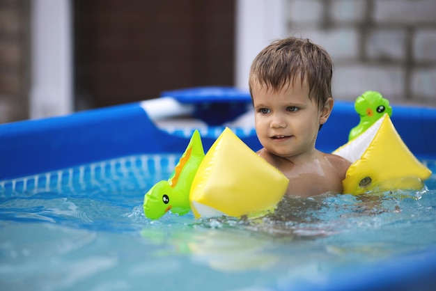 Kid in oversleeves swims in the pool in the yard